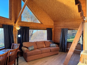 L’intérieur d’un chalet en bois, avec un canapé, une table à manger et une lampe.