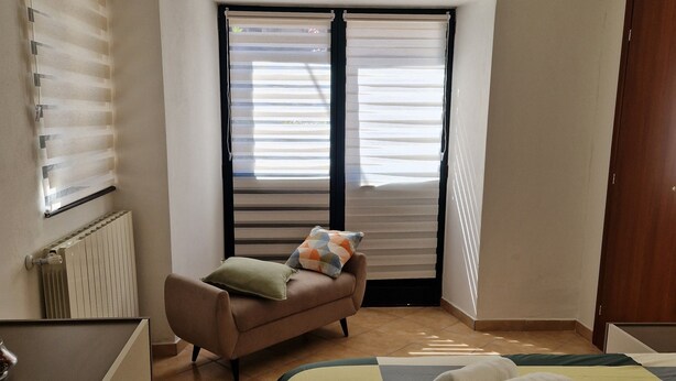 A bedroom with a bed, a sofa, a radiator, and a window with blinds. - Between Sea and Villages: your Refuge in Pogli (Pogli)