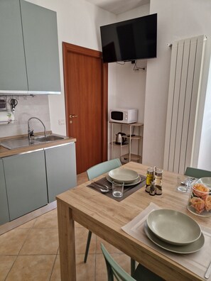 Uma cozinha compacta com pia, micro-ondas e televisão de tela plana fixada na parede.