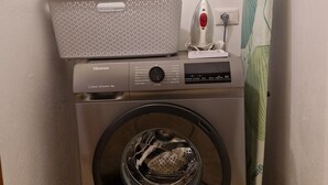 A front-loading washing machine with a basket on top, a wall-mounted ironing board, and a power outlet. - Between Sea and Villages: your Refuge in Pogli (Pogli)