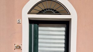 A green door with a white-framed window, a number '5' sign, and a welcome mat with a bear and cat illustration. - Between Sea and Villages: your Refuge in Pogli (Pogli)