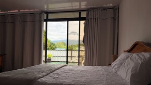 A bedroom with a large bed, a wooden headboard, and a view of a balcony with a railing and greenery. - Volcano View (San Carlos)