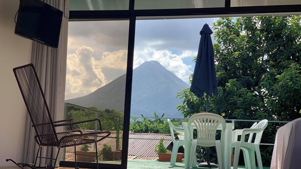 A room with a view of a mountain, a rocking chair, and a table with chairs. - Volcano View (San Carlos)