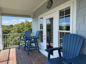 A wooden deck with two Adirondack chairs, a glass door, and a view of trees. - Views for Days! Coastal Luxury Condo w/ ICW, Marsh & Ocean Views + Pool Access (Supply)