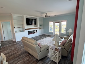 A living room with a flat-screen TV, two sofas, a fireplace, and a ceiling fan.