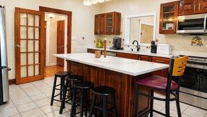 A kitchen with a large island, wooden cabinets, a refrigerator, and a microwave.
