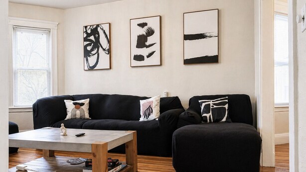 A living room with a black sofa, a coffee table, and three abstract paintings on the wall.