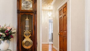 A hallway with a grandfather clock, a wooden door, and a vase of flowers.