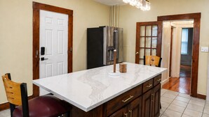 A kitchen with a marble countertop, wooden cabinets, a stainless steel refrigerator, and a pendant light.