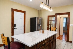 A kitchen with a marble countertop, wooden cabinets, a stainless steel refrigerator, and a pendant light. - The Artful Retreat Close to Gillette Stadium  (Boston)
