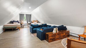 Un habitación tipo loft con cama en entrepiso, un conjunto de sofás, un aparador de madera y una silla.