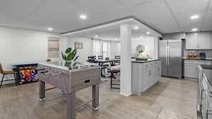 Una cocina moderna con una isla central, comedor con sillas y una mesa de futbolín.