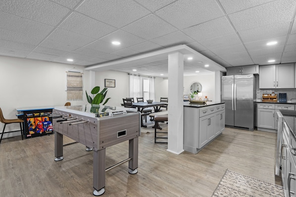 A modern kitchen with a central island, dining area with chairs, and a foosball table.
