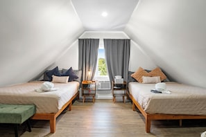 A room with two beds, a bench, a table, and a window with curtains.