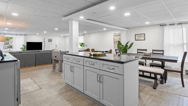 Una cocina moderna con armarios grises, un comedor con mobiliario de madera y un sofá gris.