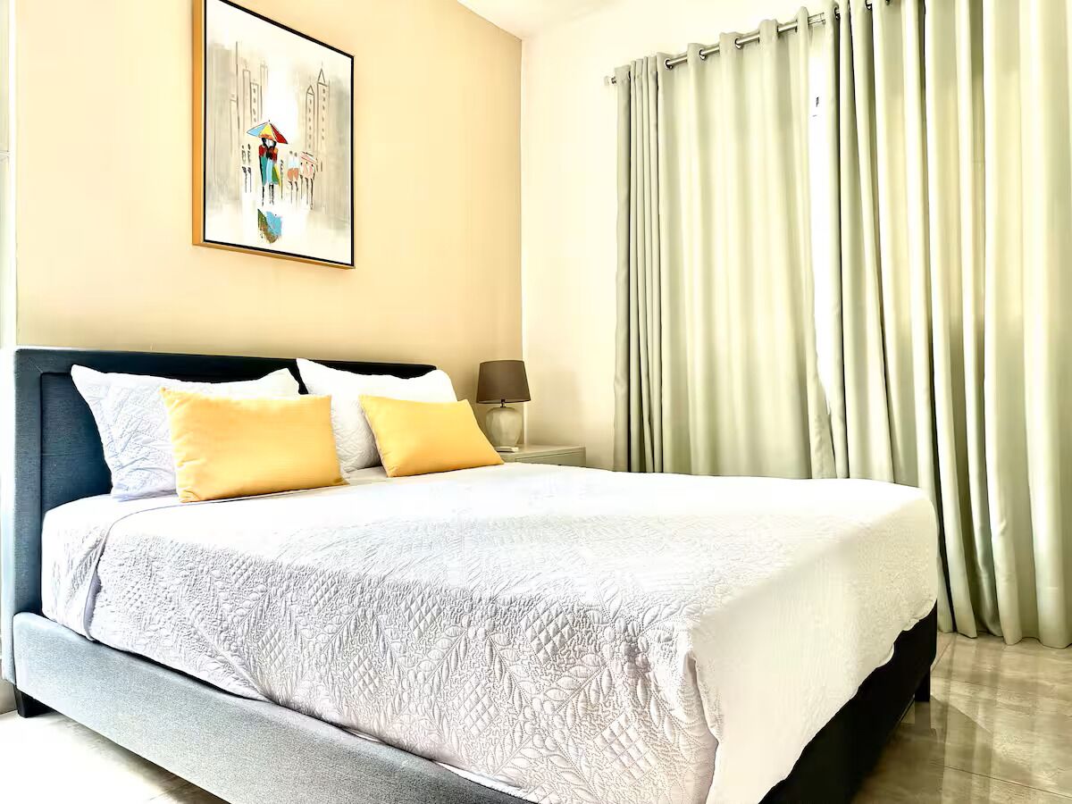 A neatly made bed with a quilted cover, a bedside lamp, and a framed picture on the wall.