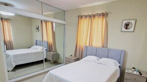 Une chambre à coucher avec un lit, une table de chevet, un miroir et un ventilateur de plafond.