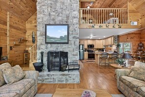 A log cabin interior with a stone fireplace, wooden walls, a dining area, and a kitchen. - Waterfront Log Cabin with Boathouse, sandy beach and firepit on Lake Anna (Bumpass)