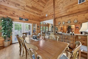 A spacious wooden dining area with a large table and chairs, a kitchen with wooden cabinets, and a large window. - Waterfront Log Cabin with Boathouse, sandy beach and firepit on Lake Anna (Bumpass)