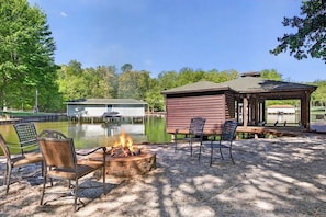 A lakeside patio with a fire pit, chairs, and a wooden structure. - Waterfront Log Cabin with Boathouse, sandy beach and firepit on Lake Anna (Bumpass)