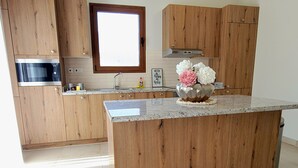 Uma cozinha com armários de madeira, micro-ondas de aço inoxidável, pia e um vaso decorativo com flores.