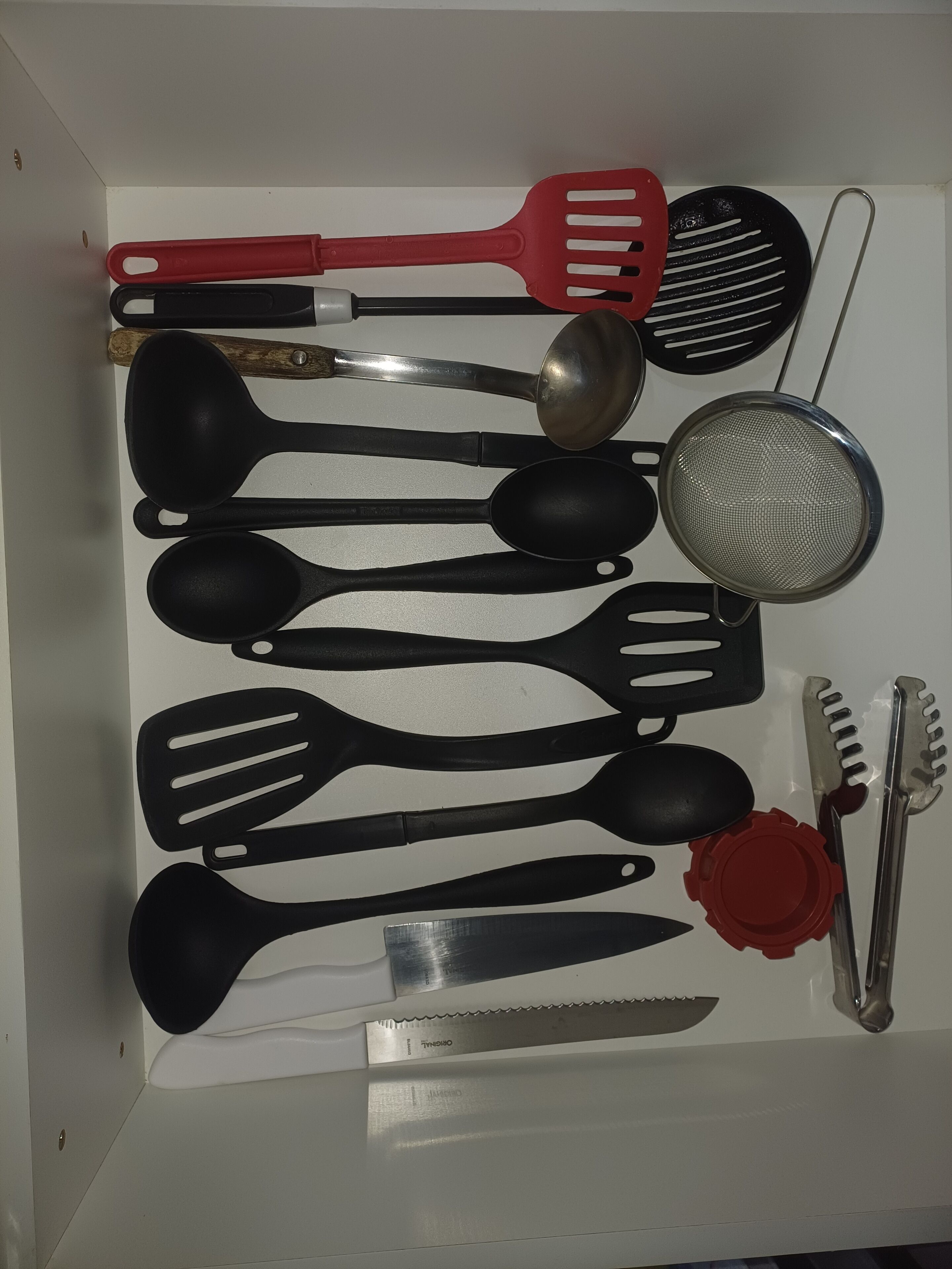 Uma gaveta com diversos utensílios de cozinha, incluindo espátulas, colheres, um escorredor e uma faca.