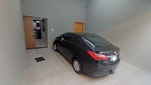 A black sedan parked in a garage with a tiled floor, a wooden door, and a light fixture on the ceiling. - Charming house near the state hospital, bakery, supermarket, and pharmacy. (franca)