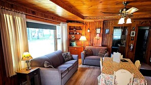 A wooden interior with a sofa, armchairs, a dining table, and a ceiling fan.
