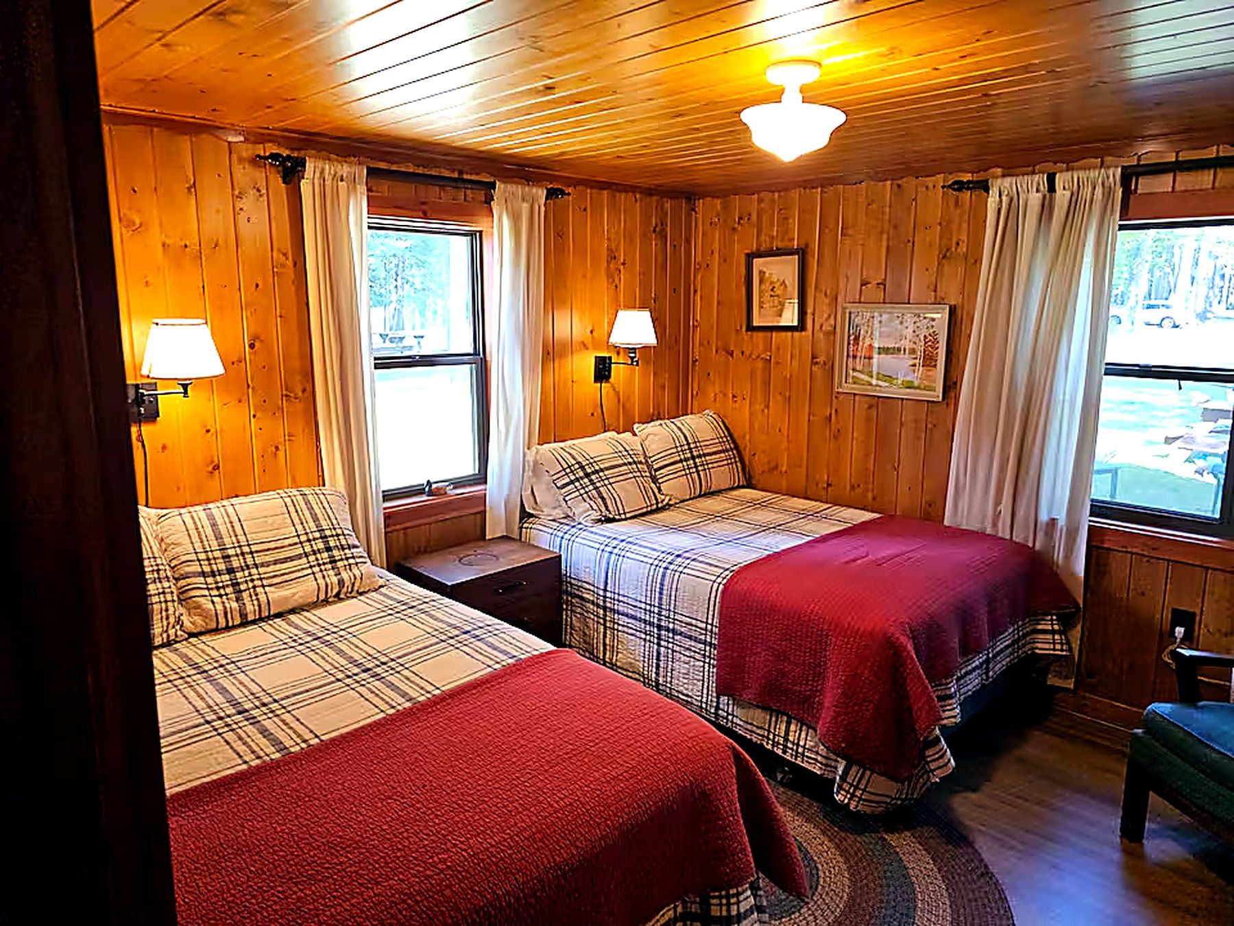 A cabin-style room with two beds, wooden walls, and a large window.