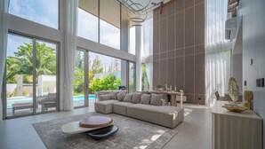 A modern living room with a sectional sofa, a coffee table, and a view of a swimming pool. - GRAND VIEW Residences Villa with Pool (Choeng Thale)