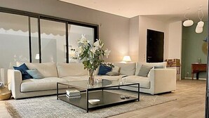Ein modernes Wohnzimmer mit einer Sofagarnitur, einem Glastisch und einem großen Fenster.
