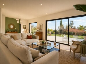 Uma sala de estar espaçosa com um sofá grande, uma mesa de centro e vista para um jardim através de amplas portas de correr.