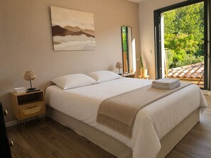 A bedroom with a large bed, a bedside table, a lamp, a mirror, and a view of greenery outside. - Contemporary villa with pool near Aix-en-Provence (Éguilles)