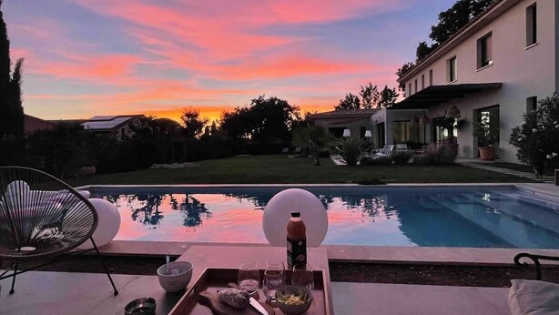 Ein Poolbereich mit Sonnenuntergangblick, ein Esstisch mit Besteck und ein Stuhl.
