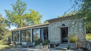 Una casa de pedra amb una gran finestra de vidre, una escala de pedra i un jardí.
