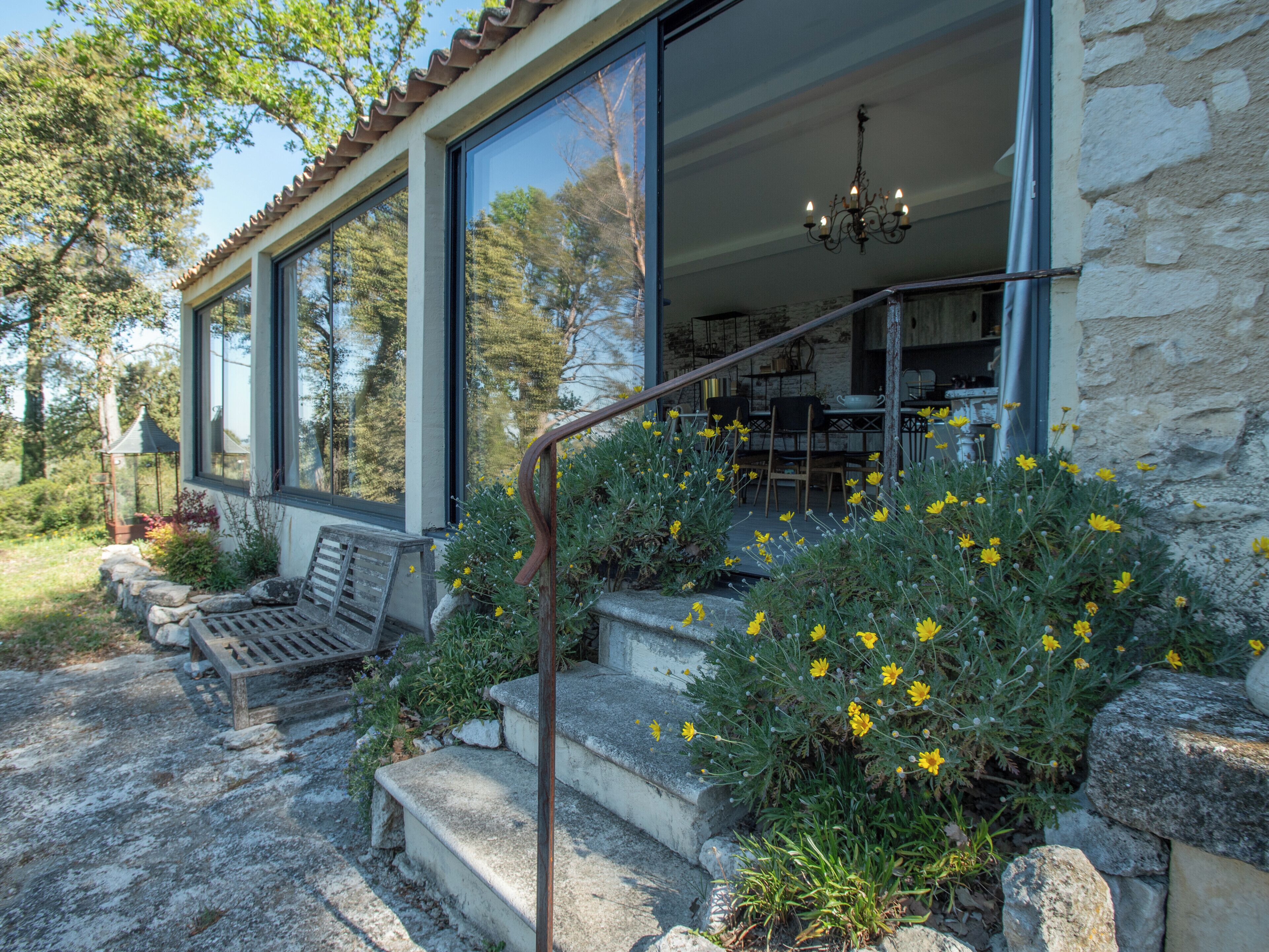 A stone house with a porch, outdoor seating, and yellow flowers.