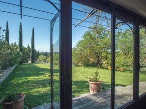 Une véranda offrant une vue sur un jardin bien entretenu, comprenant une pelouse, des arbres et un étang.
