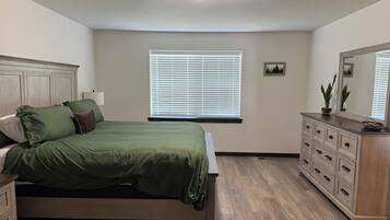 A bedroom with a bed, dresser, window with blinds, and a ceiling light.