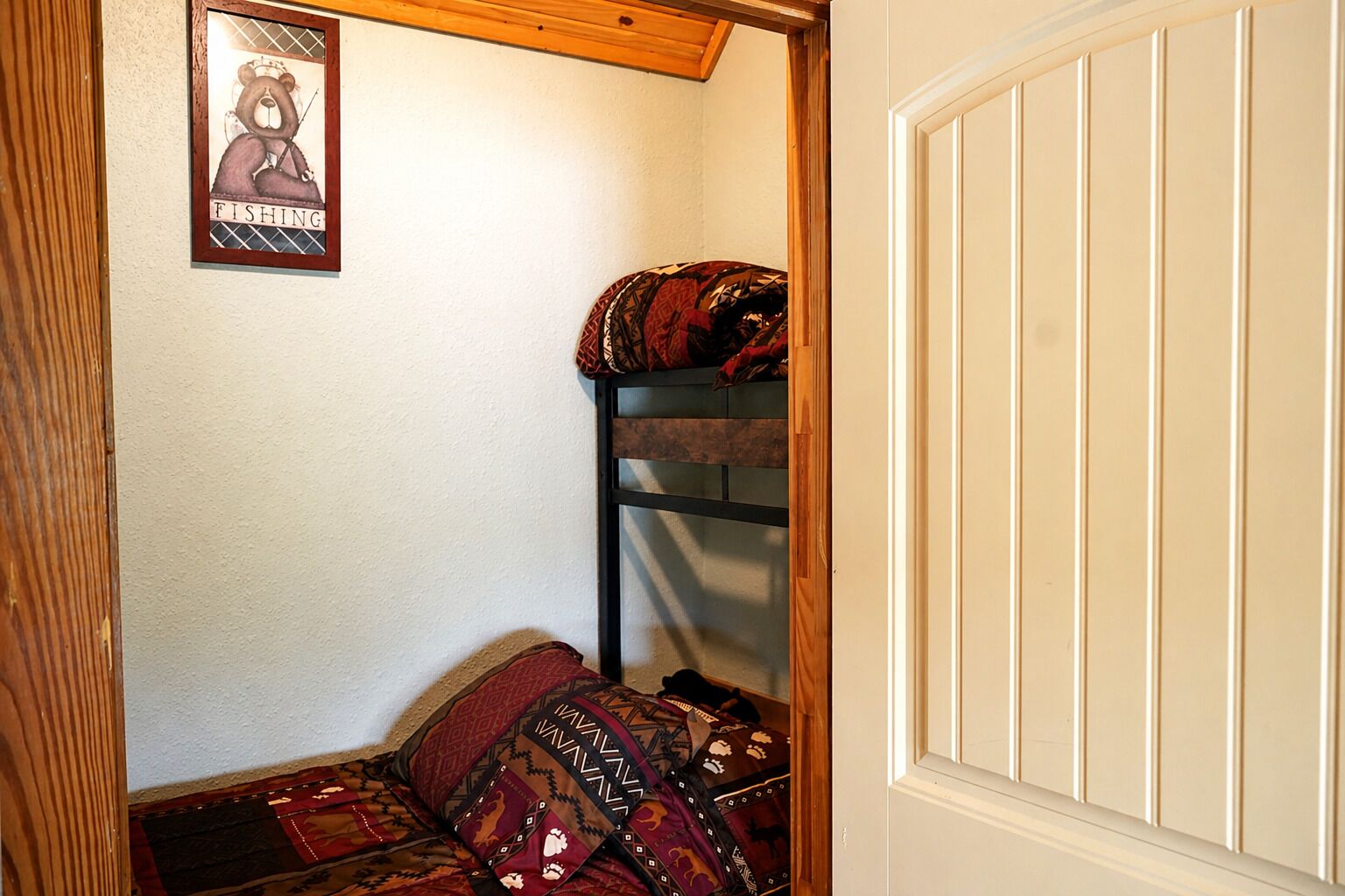 Une chambre d’angle avec un lit superposé, un tableau encadré au mur et une porte.