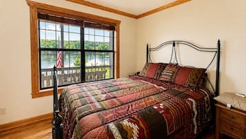 Una camera da letto con un'ampia finestra, un letto con biancheria a motivi, un comodino e un pavimento in legno.