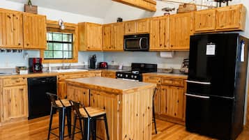 Una cucina con mobili in legno, un frigorifero nero, un forno a microonde, un piano cottura e due sgabelli da bar.