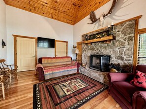 Ein gemütliches Wohnzimmer mit Kamin aus Stein, Holzboden und einem karierten Sofa.
