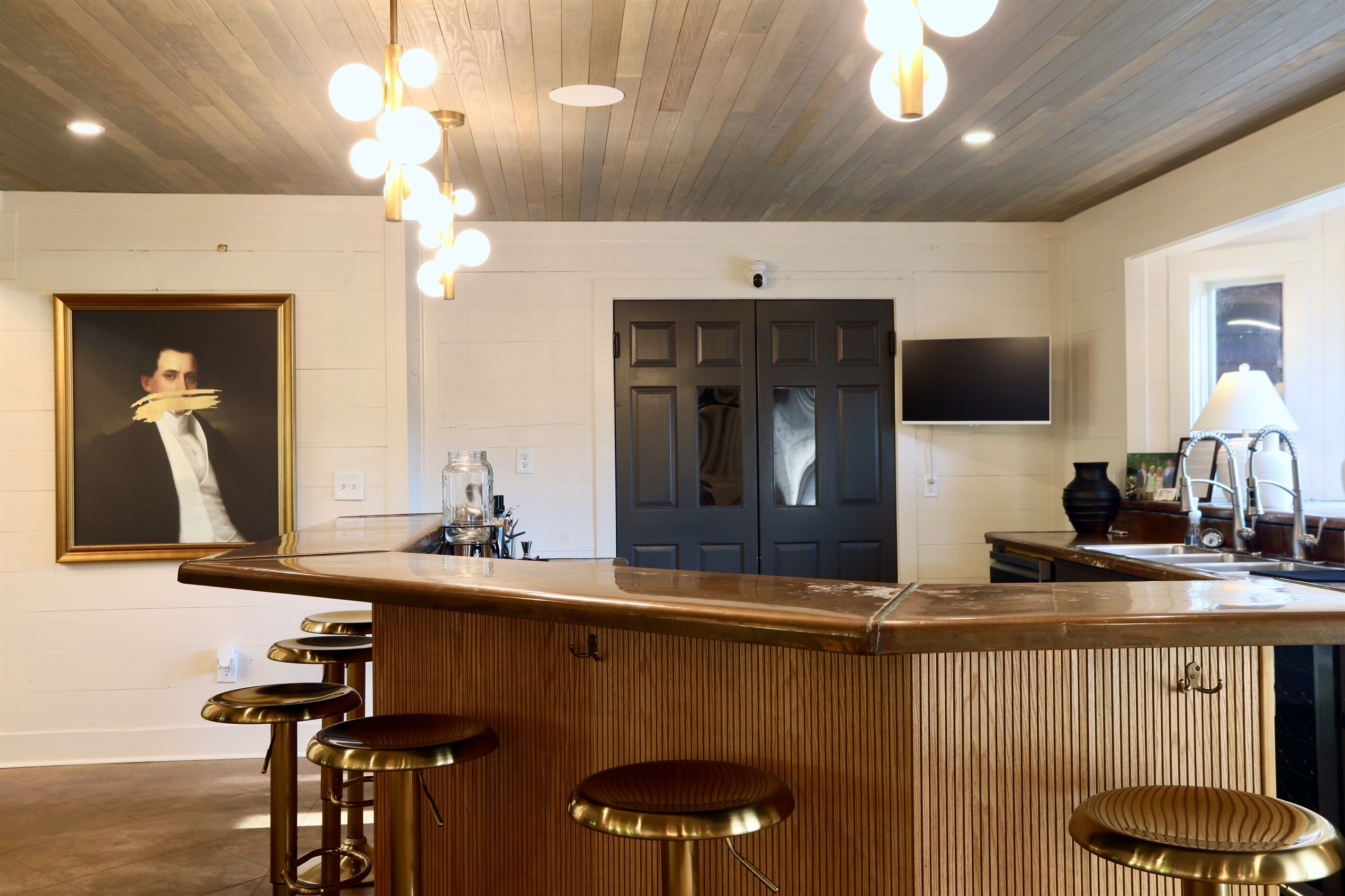 Une cuisine avec un bar en bois, des tabourets, un tableau, une télévision et une porte.