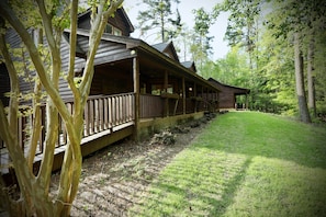 A log cabin with a porch, surrounded by trees and a grassy yard.