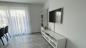 Un saló modern amb un televisor de pantalla plana, un moble blanc per a l'electrònica i una zona de menjador amb cadires.