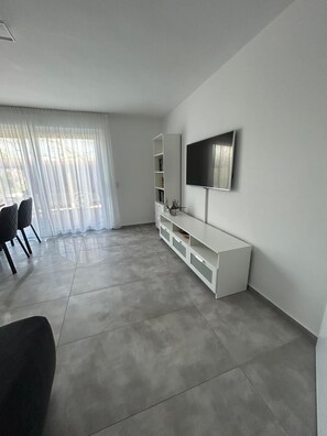 Un saló modern amb un televisor de pantalla plana, un moble blanc per a l'electrònica i una zona de menjador amb cadires.