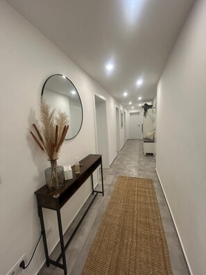 Un couloir avec une console, un miroir et un vase contenant des plantes séchées.