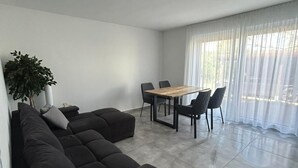 Un saló modern amb un sofà modular, una taula de dinar amb cadires, una planta en test i grans finestres amb cortines primes.