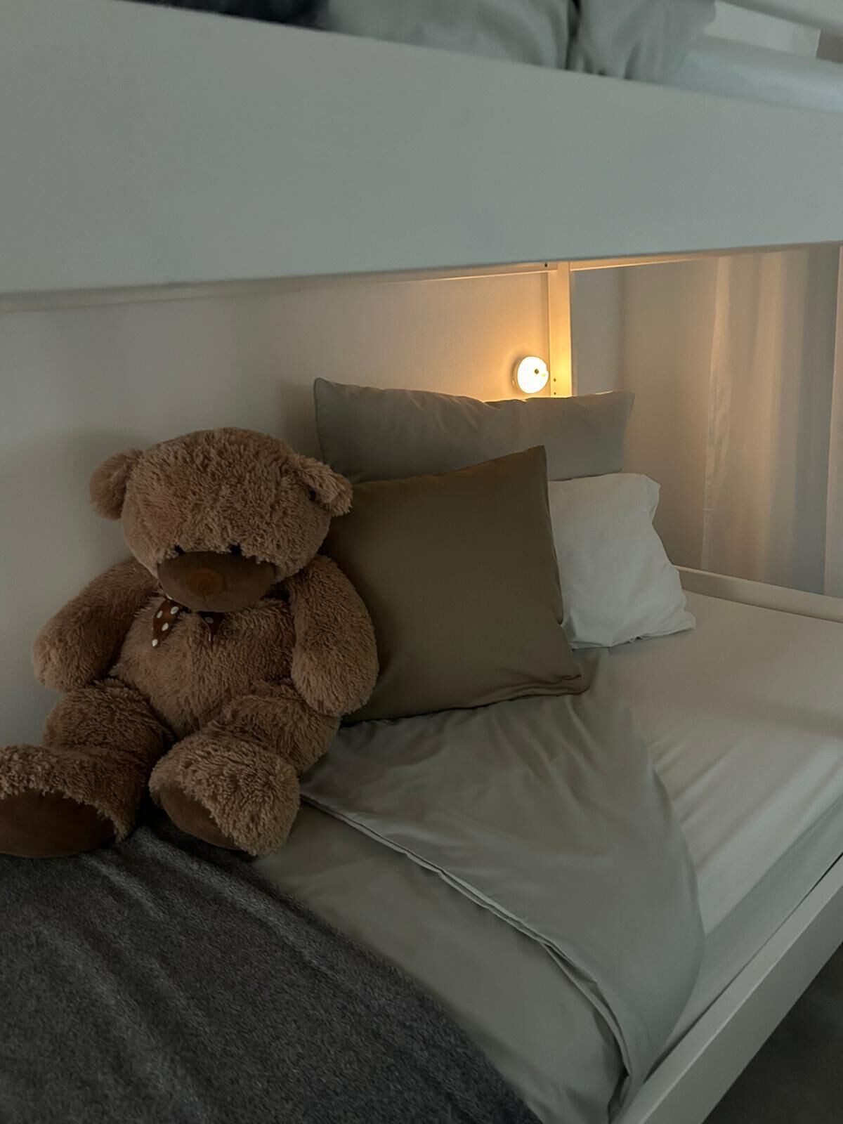Ein Stockbett mit einem Teddybären auf der Unterliege, einem Kissen und einer Nachttischlampe.