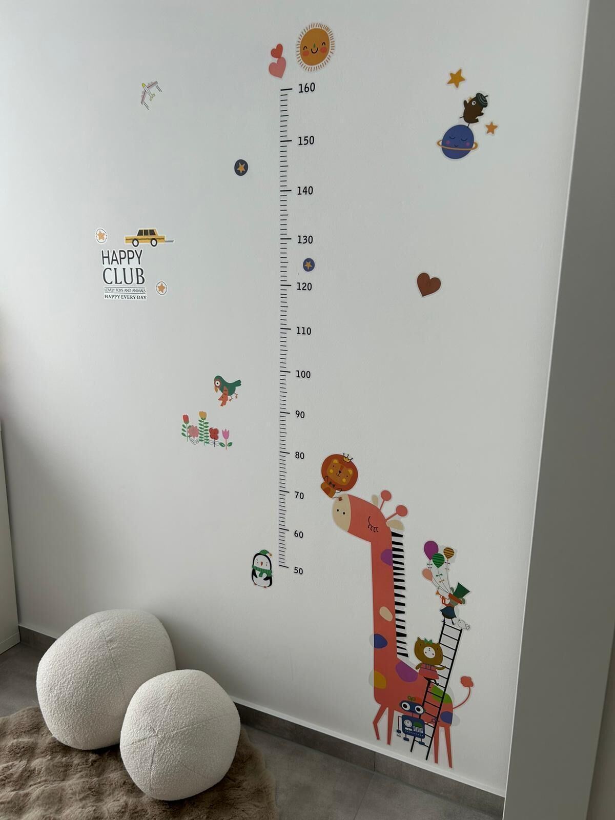 Una pared con una tabla de medidas de altura y diferentes pegatinas, incluyendo una jirafa y un gato.
